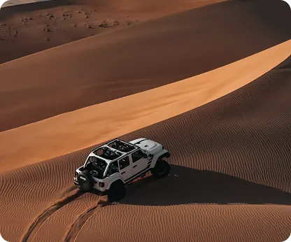 A white 4x4 on a rippled dune with its tracks curving away behind it