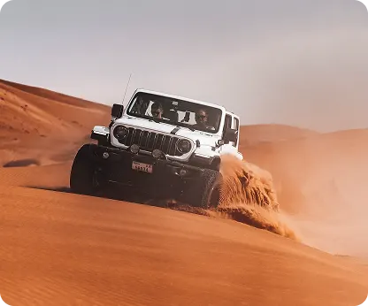 A white Jeep Wrangler coming over a dune crest with two guests inside