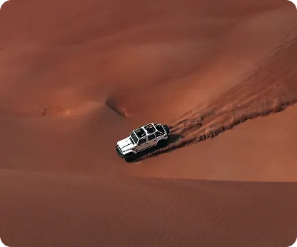 Seen from above, a white 4x4 descending a deep red dune