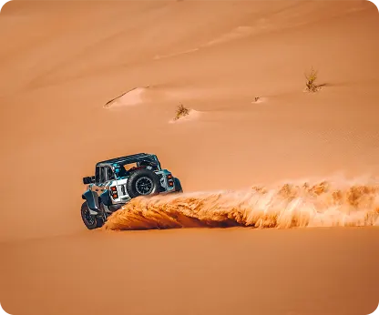 A dark 4x4 traversing a long dune slope in low evening light