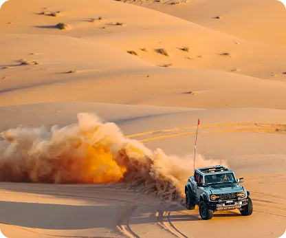 A 4x4 trailing a cloud of sand across the dunes in golden late-afternoon light