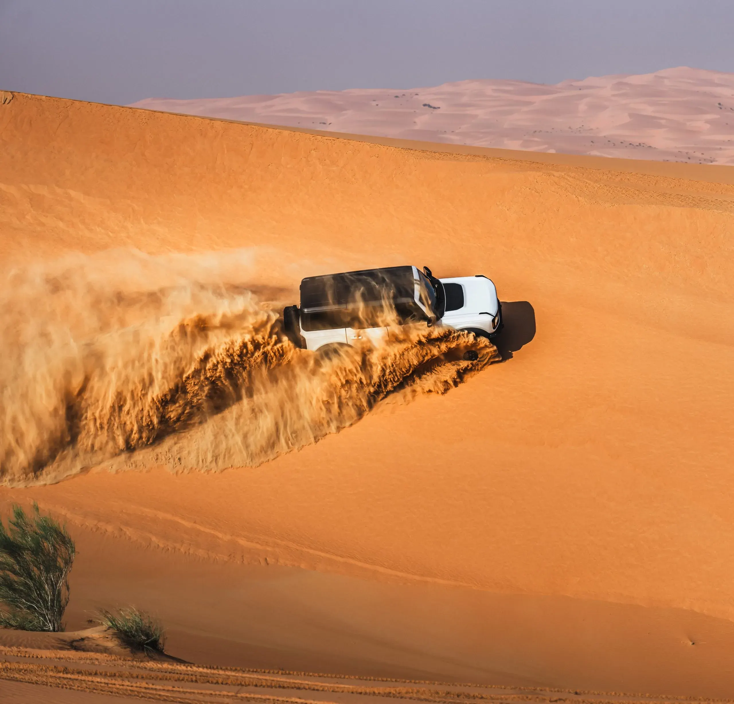 A white 4x4 throwing up a long plume of sand as it drops down a steep dune face