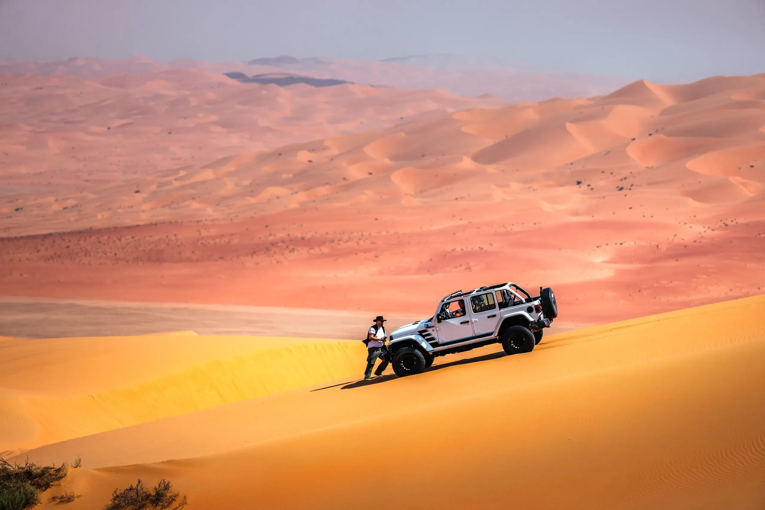 A guide standing beside a white 4x4 parked on a dune ridge, with rolling dunes behind