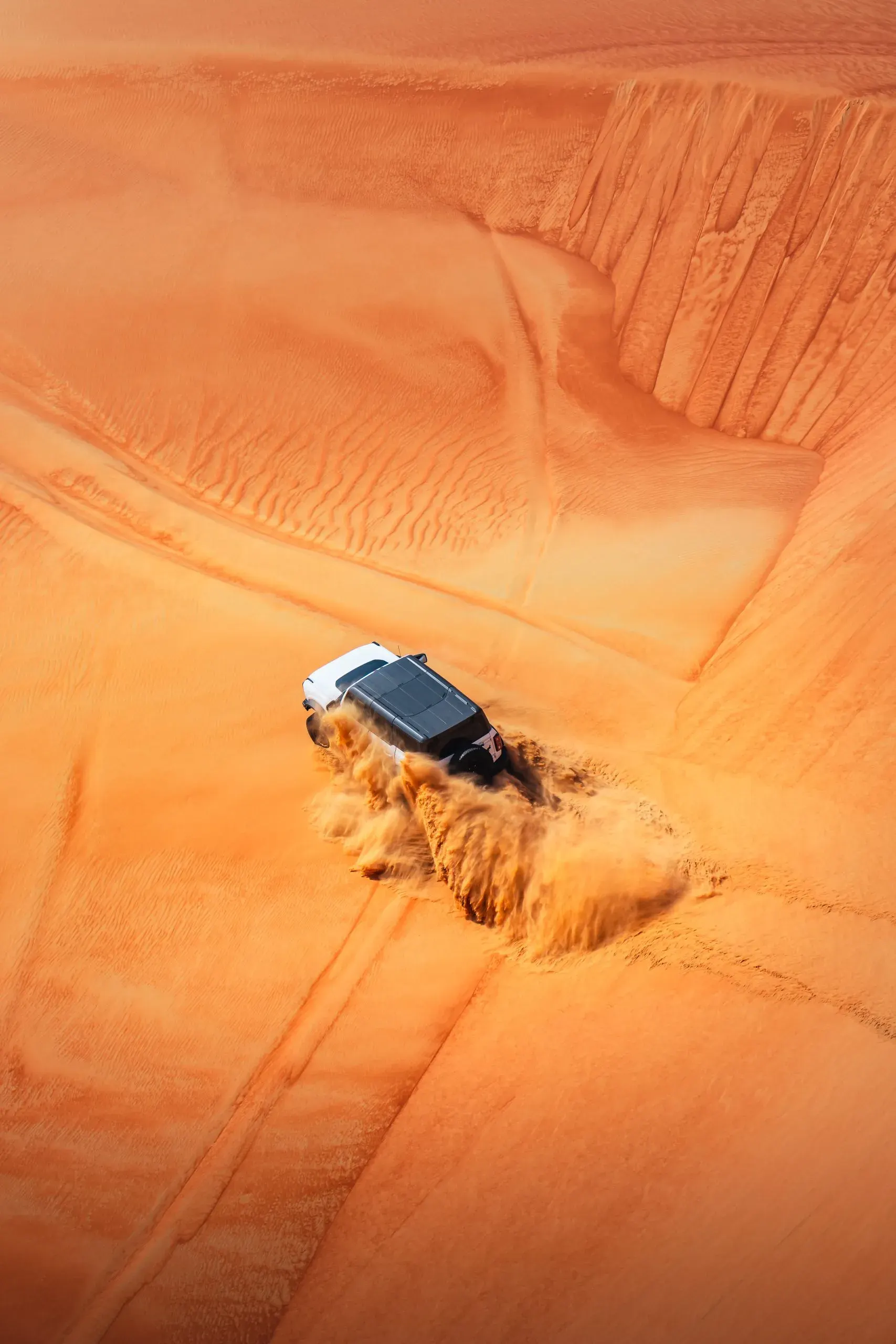 Seen from directly above, a white 4x4 throwing up sand as it turns on an orange dune